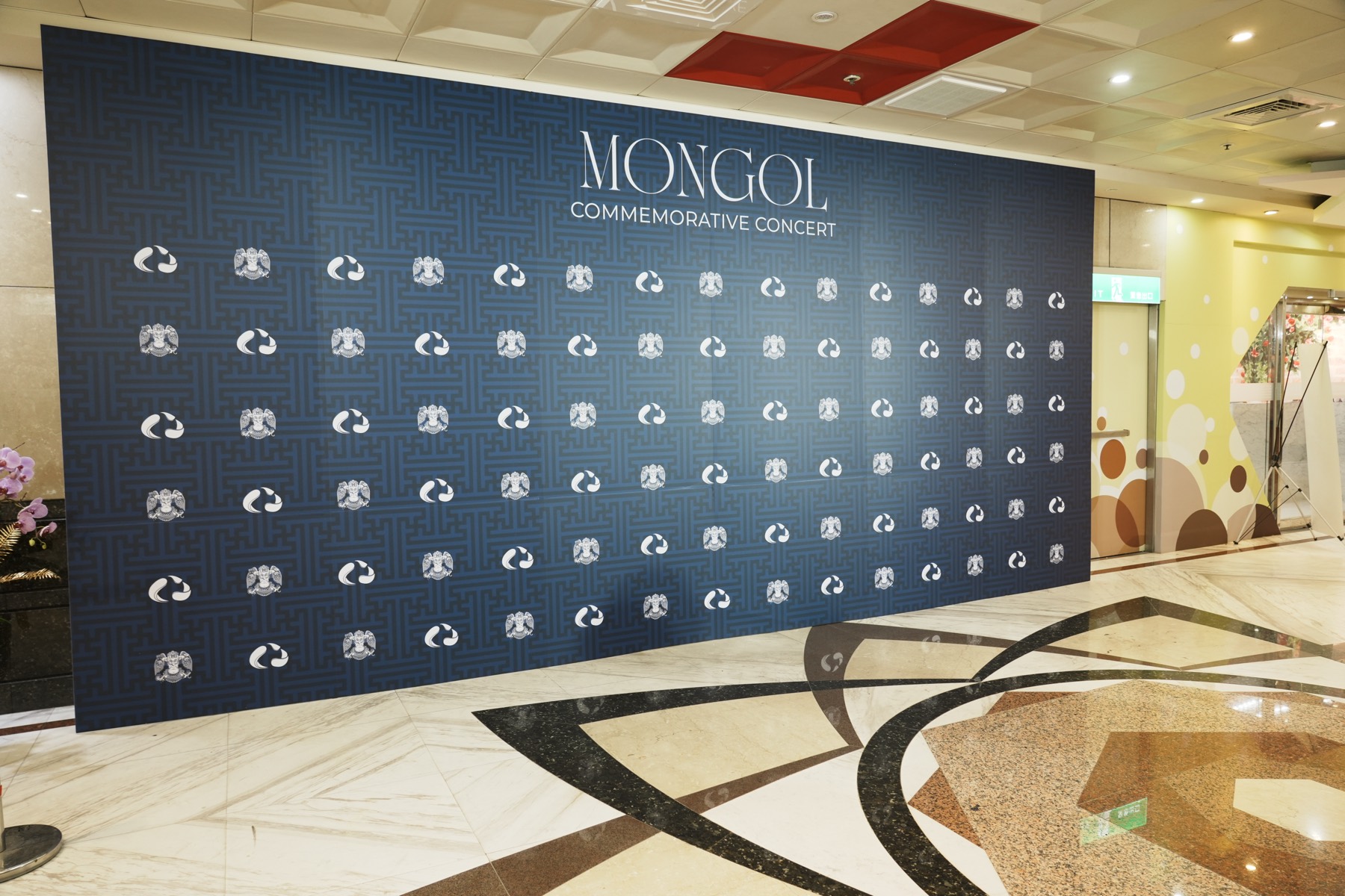 The navy Mongol Commemorative Concert backdrop wall, patterned with coin seals, installed at the venue