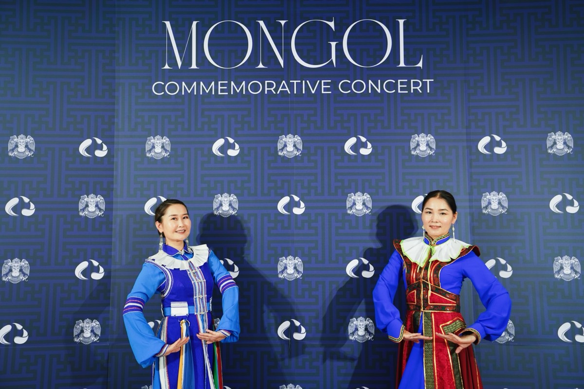 Two dancers in traditional Mongolian dress in front of the backdrop photo wall